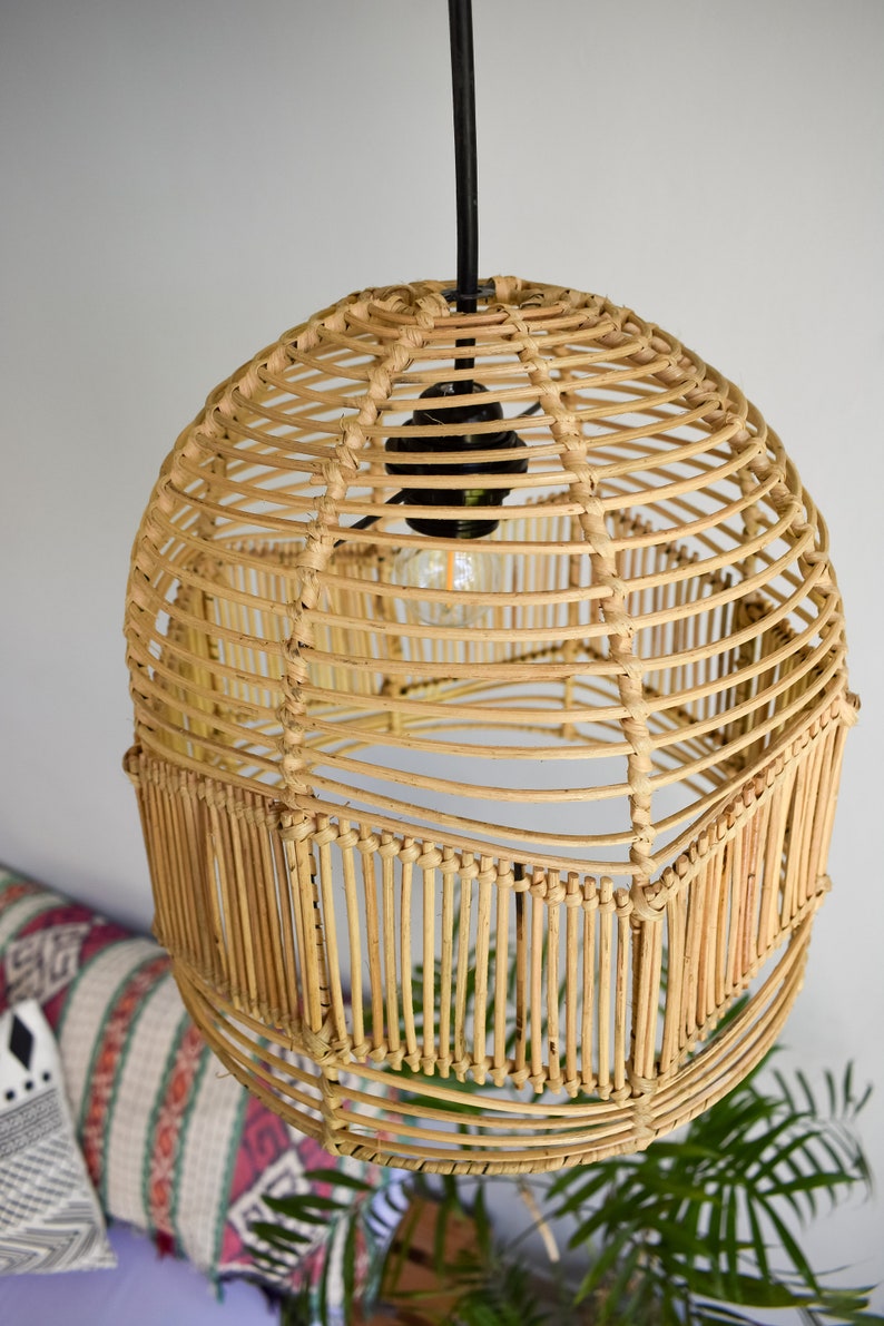 May include: A round, woven rattan pendant light fixture with a black cord and a light bulb. The light fixture is hanging from the ceiling and is surrounded by a white wall.