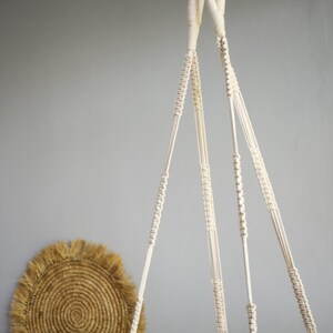 May include: A white macrame plant hanger with three strands of rope hanging from a silver chain.