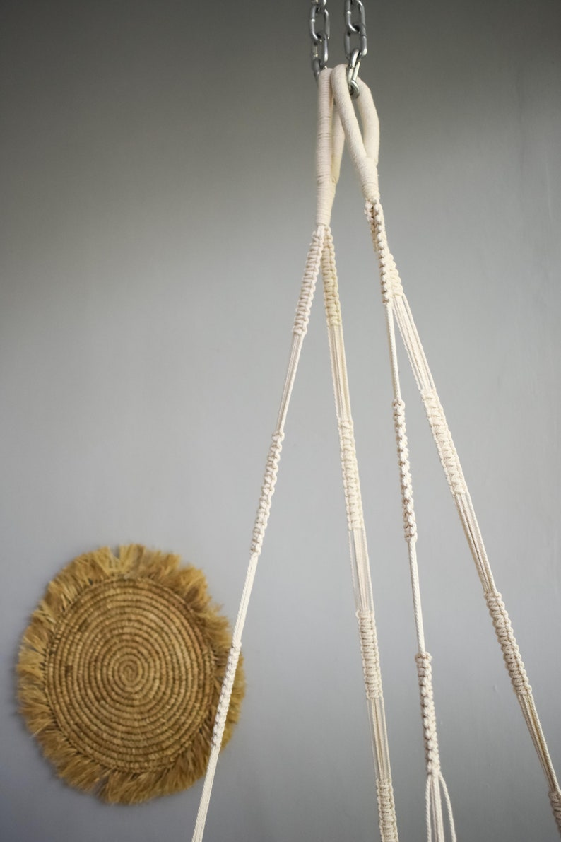 May include: A white macrame plant hanger with three strands of rope hanging from a silver chain.