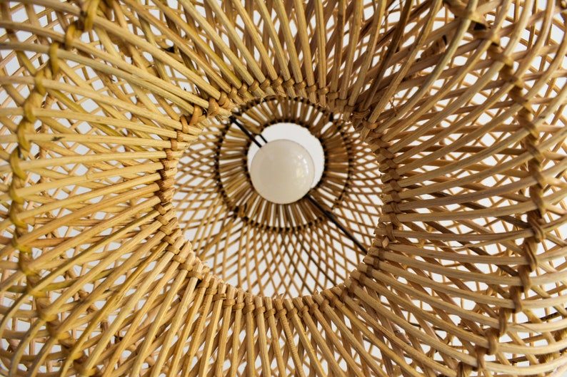 May include: A close-up view of a woven wicker lampshade with a white light bulb inside. The lampshade is made of natural materials and has a warm, rustic look.