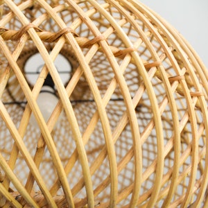May include: A close-up of a woven wicker lampshade. The shade is made of natural, light brown rattan and has a circular shape.