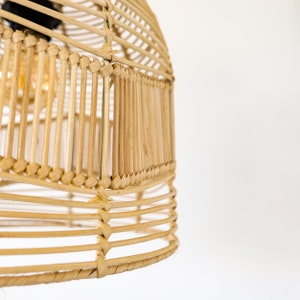 May include: A natural woven pendant light fixture made of light brown rattan. The light fixture has a round shape and is made of thin strips of rattan woven together.