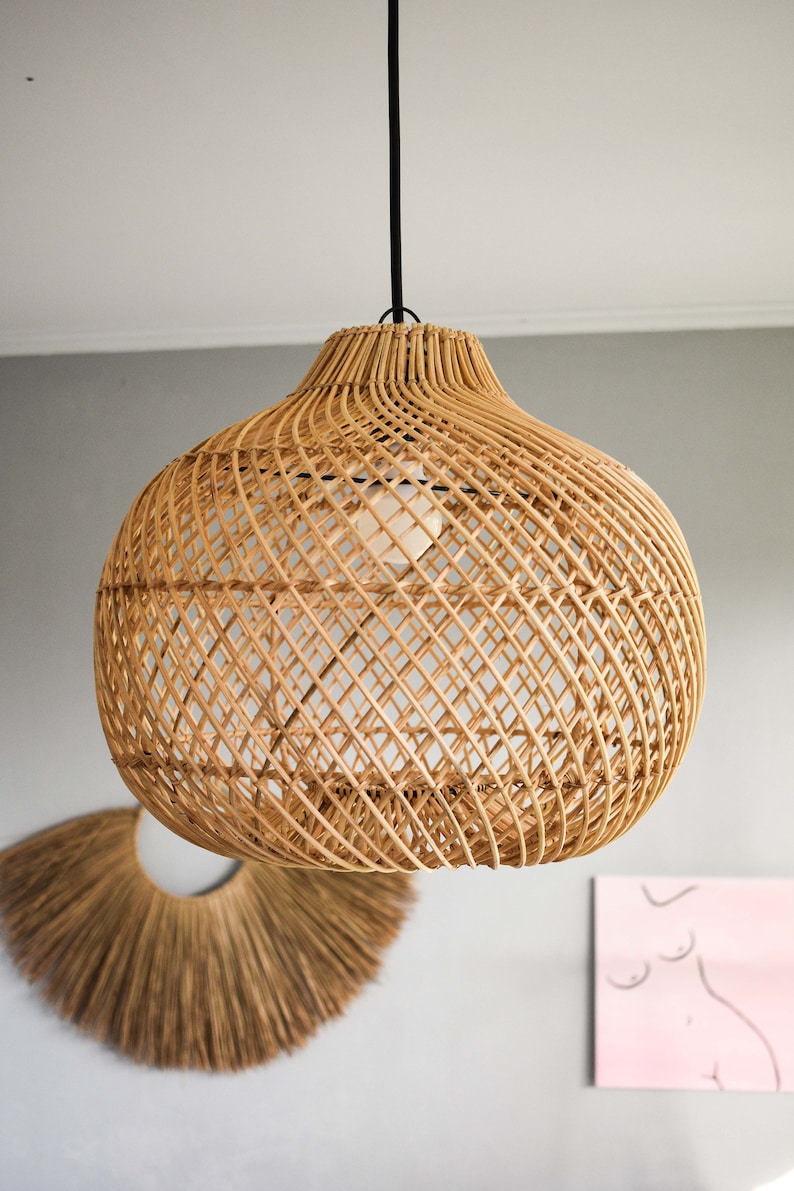 May include: A woven rattan pendant light fixture with a round, bulbous shape. The light fixture is hanging from a black cord.