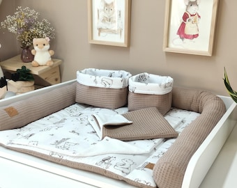 May include: A baby changing mat set featuring a taupe waffle-textured fabric and a white cotton lining with a black line-art animal print. The set includes two rectangular storage baskets, a padded mat with raised sides, and a folded square blanket.