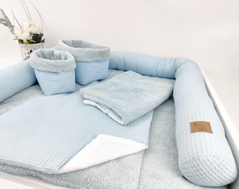 May include: A light blue waffle-textured fabric set including a long cylindrical bumper, two storage baskets, and a folded blanket. The items feature a soft, plush white lining and a small brown leather-like patch with an elephant icon.