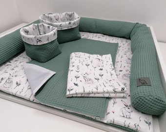 May include: A green and white baby play mat with a removable, padded border. The mat features a white fabric with a repeating pattern of small white bunnies and green leaves. The mat also includes two green waffle-weave storage baskets and a white, quilted, rectangular pillow.