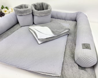 May include: A gray waffle weave baby nest with a gray waffle weave bolster pillow, two gray waffle weave baskets, and a gray waffle weave towel. The bolster pillow has a small gray elephant logo.