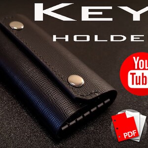 Peut inclure: Porte-clés en cuir noir avec une fermeture à pression et un bouton en métal. Le porte-clés est plié et comporte une rangée de boucles métalliques pour les clés. L'image comprend le texte "KEY HOLDER" et un logo YouTube.