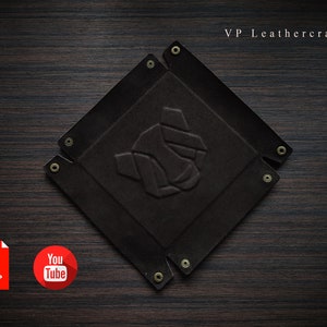 May include: A dark brown leather tray with a square shape and rounded corners. The tray has a raised embossed design in the center and is secured with gold-colored rivets around the edges. The tray is on a dark wood surface. VP Leathercraft is written in white text at the top of the image.