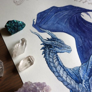 May include: A watercolor painting of a blue dragon with a starry sky pattern on its wings. The dragon's head is turned to the side, and its eyes are closed. The painting is surrounded by crystals.
