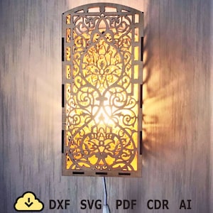 May include: A wooden wall sconce with an intricate, laser-cut design. The sconce has a rectangular shape with an arched top and features a warm, glowing light emanating from within. The design includes floral and geometric patterns. The image also includes the text "DXF SVG PDF CDR AI".