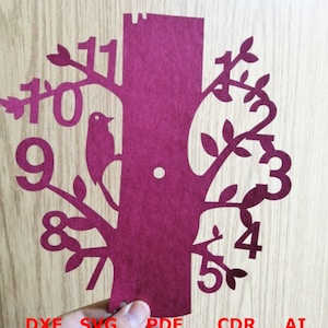 May include: A burgundy paper cutout of a tree with a bird and the numbers 1 through 12 around the tree. The tree is a silhouette with a thick trunk and branches. The bird is perched on a branch. The numbers are in a simple font and are placed around the tree in a circle.
