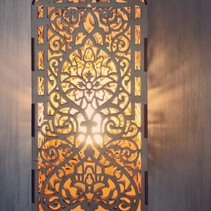 May include: A wooden wall sconce with an intricate, laser-cut floral design. The sconce is rectangular with a curved top and emits a warm, inviting light. The light shines through the detailed patterns, creating a decorative and artistic effect.