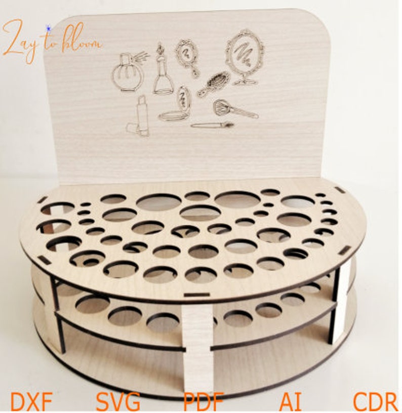 Pu&ograve; includere: Organizzatore per trucco in legno con base circolare e tre livelli di fori rotondi. L'organizzatore ha un pannello posteriore con un design decorativo di pennelli per il trucco, bottiglie e specchi. Il testo "Zay to bloom" &egrave; stampato sul pannello posteriore.