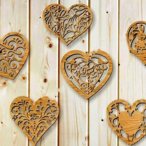 Puede incluir: Cinco adornos de madera en forma de corazón con intrincados diseños recortados. Los adornos están hechos de madera marrón claro y tienen un acabado natural.
