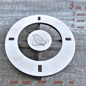 Può includere: Un cerchio di legno con un disegno di un uccello al centro. Il cerchio ha tre anelli concentrici, ognuno con uno spessore diverso: 3 mm, 4 mm e 6 mm. Il testo "3 in 1" è scritto sopra il cerchio. Il testo "DXF SVG PDF CDR AI" è scritto sotto il cerchio.