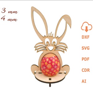 Könnte beinhalten: Ausgeschnittener Holzhase mit einer Dicke von 3 mm und 4 mm. Der Hase hält ein verziertes Osterei. Der Hase ist ein Ständer für ein Osterei.