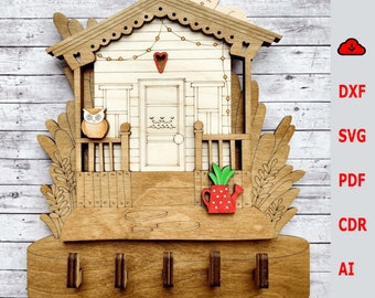 May include: Wooden key holder shaped like a house with a porch, a red heart, and a small owl. The house has a white door and a window with a floral design. There are five hooks on the bottom of the house.