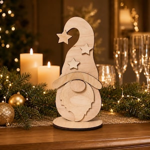 Può includere: Una statuetta di gnomo in legno chiaro con un cappello alto e curvo decorato con tre ritagli a forma di stella. Lo gnomo ha un naso rotondo e una barba strutturata, il tutto montato su una base circolare. La venatura del legno è visibile.