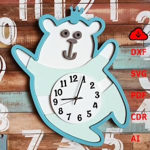 Puede incluir: Un reloj de madera azul y blanco con forma de oso con una corona en la cabeza. La esfera del reloj tiene números y manecillas negros. El oso lleva una camisa a rayas azules y blancas.