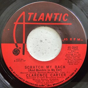 May include: A vinyl record with a red and brown label. The label displays the word "ATLANTIC" and the song title "SCRATCH MY BACK" by Clarence Carter. The label also includes details such as the recording studio and the record's speed, 45 RPM.