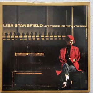 May include: Album cover for Lisa Stansfield's "Live Together (New Version)". The image shows a person in a red jacket with black stripes, a matching hat, and blue jeans. The background is dark with a bench and a fence.