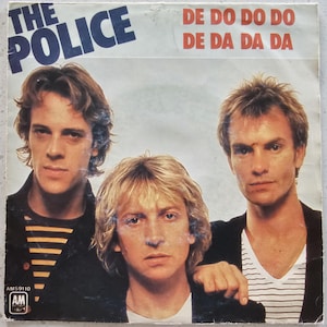 May include: Vintage vinyl record sleeve for The Police, featuring three band members. The band's name is in blue, with the song title "De Do Do Do, De Da Da Da" in red. The record label is AM Records.