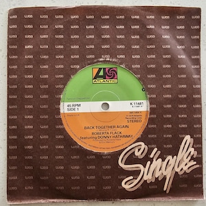 May include: A vintage 45 RPM vinyl record single of "Back Together Again" by Roberta Flack featuring Donny Hathaway. The record label is green and orange with the Atlantic Records logo. The sleeve is brown with a repeating "wea" pattern.