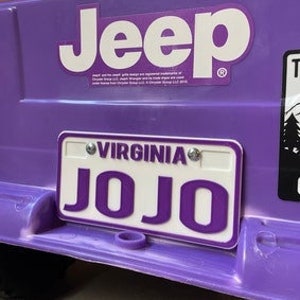 May include: Purple toy Jeep with a white "Jeep" logo and a white license plate that says "VIRGINIA JO JO" in purple letters.