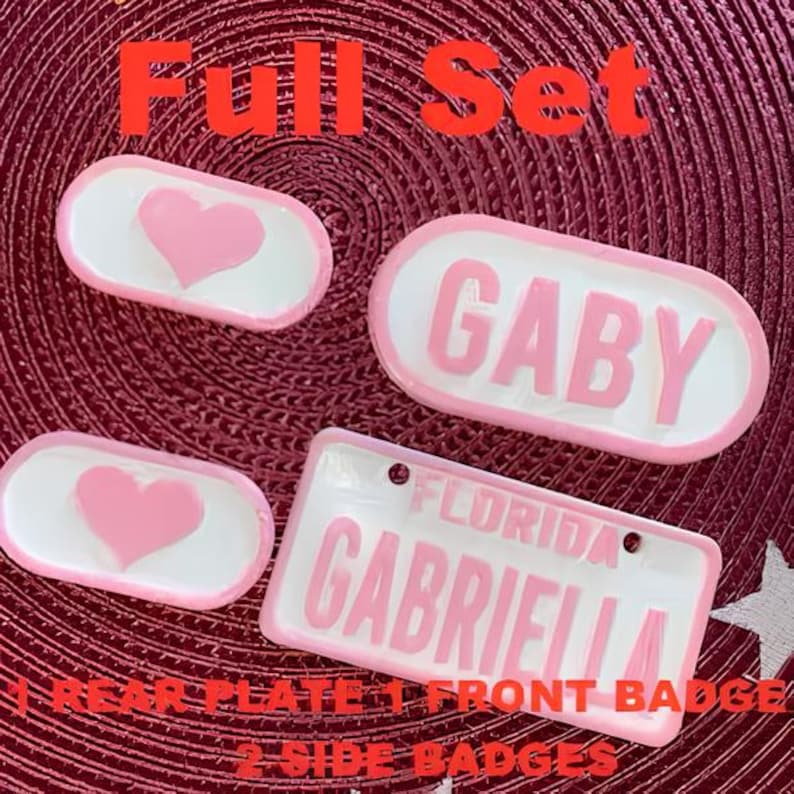 Puede incluir: Conjunto completo de placas de matr&iacute;cula y placas laterales de coche rosas y blancas. La placa delantera dice "Gaby" y la placa trasera dice "Florida Gabriella". Las placas laterales tienen un dise&ntilde;o de coraz&oacute;n.