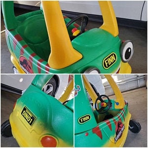 Puede incluir: Coche de juguete de pl&aacute;stico verde y amarillo con volante, una pegatina de dinosaurio y el nombre "FINN" en el lateral. El coche tiene un dise&ntilde;o de rayas rojas y amarillas.