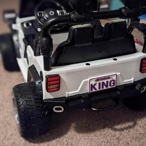 May include: White toy jeep with black wheels and a black roll bar. The jeep has a purple license plate that says "KING".