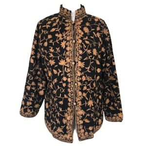 Puede incluir: Chaqueta negra con intrincado bordado floral dorado. La chaqueta presenta un cuello mandarín y una botonadura frontal. El diseño floral cubre toda la chaqueta, creando un aspecto detallado y elegante. Una elegante prenda de abrigo.