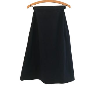 May include: A solid black skirt hangs from a wooden hanger against a white background. The skirt has a simple, flowing design, with a slightly flared shape. The fabric appears to be a medium-weight material.