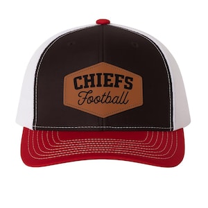 May include: A Chiefs football cap with a red bill and button, a brown and white mesh back, and a brown patch with the words "CHIEFS Football". The cap is a classic baseball style.