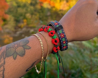 Può includere: Un set di quattro braccialetti, uno con un motivo floreale nero e rosso, due con fiori rossi e verdi e un braccialetto a catena dorata.