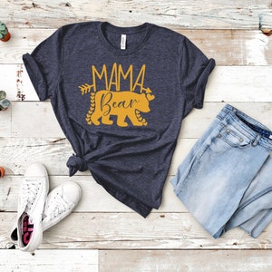 May include: A navy blue t-shirt with a gold graphic of a bear with the text "Mama Bear" and an arrow.