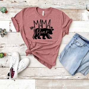 May include: A mauve t-shirt with a black graphic of a bear with the text "Mama Bear" and an arrow pointing to the right. The bear is surrounded by small hearts.