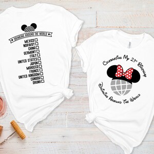 Op de afbeelding: Twee witte T-shirts met een Mickey Mouse-ontwerp. Eén shirt zegt "Drinking Around the World" met een lijst van landen en vinkjes. Het andere shirt zegt "Celebrating My 21st Birthday Drinking Around the World".