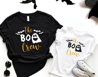 May include: Two black and white t-shirts with the text "The Boo Crew" in gold lettering and a white ghost with a smiling face. The shirts are on a white background with black bats.