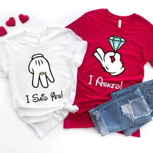 May include: Two white t-shirts with a cartoon hand design. One shirt says "I Said Yes!" and the other says "I Asked!"