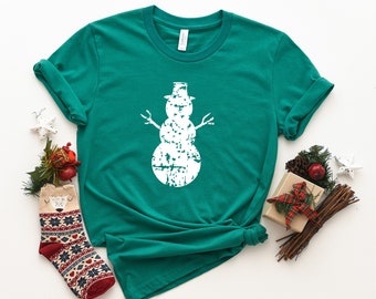 May include: A green t-shirt with a white distressed snowman graphic. The snowman has a hat and two sticks for arms.