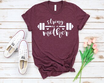 May include: A maroon t-shirt with the text "strong as a mother" and a barbell graphic printed in white.