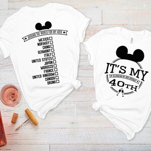 May include: Two white t-shirts with black text and a Mickey Mouse ear design. The first shirt says "Around the world for my 40th" with a list of countries. The second shirt says "It's my 40th celebrating my 40th birthday".