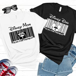 以下が含まれることがあります： 黒い文字とグラフィックが描かれた白いTシャツ2枚。左側のシャツには「Disney Mom」とバーコードとリボンが付いたミッキーマウスの頭が書かれている。右側のシャツには「Disney Dad」とバーコードとサングラスをかけたミッキーマウスの頭が書かれている。