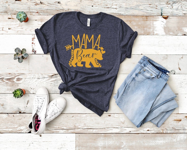 May include: A navy blue t-shirt with a gold graphic of a bear with the text "Mama Bear" and an arrow.