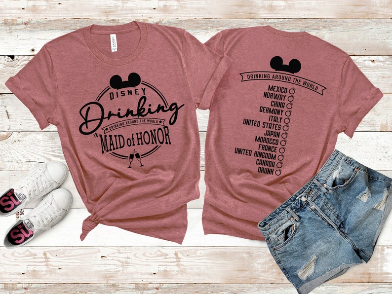 Może przedstawiać: R&oacute;żowy T-shirt z czarnym nadrukiem, na kt&oacute;rym widnieje napis "Disney Drinking" z głową Myszki Miki i tekst "Drinking Around the World" w k&oacute;łku. Pod k&oacute;łkiem znajduje się napis "Maid of Honor". Na plecach T-shirtu znajduje się czarny nadruk z napisem "Drinking Around the World" z głową Myszki Miki i listą kraj&oacute;w.