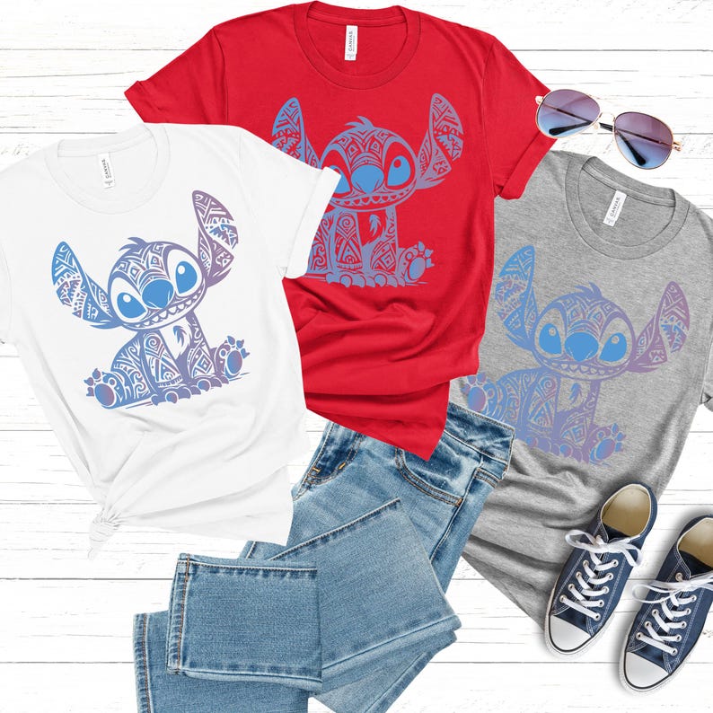 K&ouml;nnte beinhalten: Drei T-Shirts mit einem blauen Stitch-Charakter mit einem Tribal-Muster-Design. Die Shirts sind wei&szlig;, rot und grau. Die Shirts liegen auf einer Holzoberfl&auml;che mit einer Sonnenbrille und zwei Paar Turnschuhen.