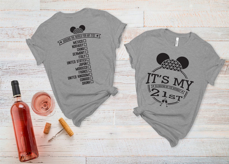 May include: Two gray t-shirts with black text and graphics. The first shirt says "Around the world for my 21st" with a list of countries and checkboxes. The second shirt says "It's my 21st" with a Mickey Mouse head and a champagne glass graphic.