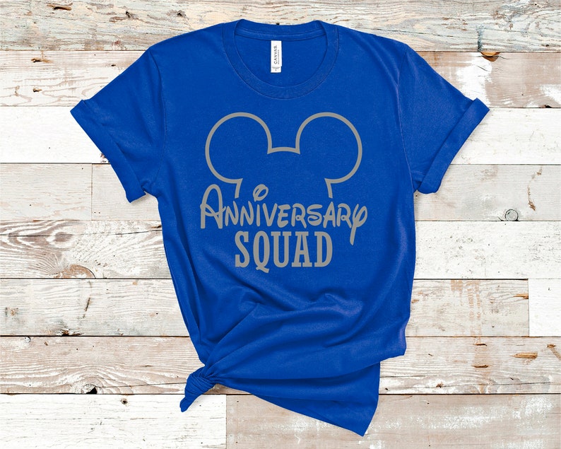 May include: A bright blue t-shirt with a grey Mickey Mouse head outline and the words "Anniversary Squad". The shirt is knotted at the bottom. The background is a light wood-grain surface.